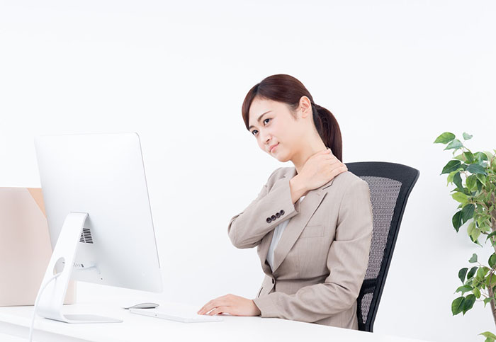 椅子に座ってパソコンに向かい肩を痛そうに触っている女性
